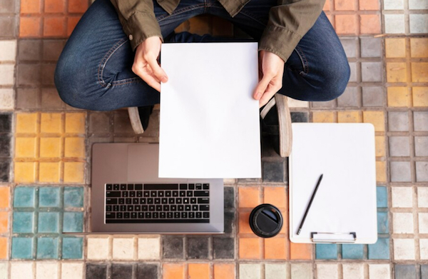 Imagen de una persona sentada en el piso con una libreta en sus manos y una computadora portátil.